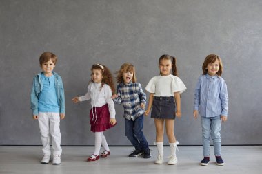 Modern bir stüdyoda gündelik kıyafetlerle eğlenen bir grup mutlu aktif çocuk. Bir grup neşeli küçük çocuk komik suratlar yapıyor, etrafta takılıyor ve fotoğraf çekimi sırasında farklı duygular gösteriyorlar.