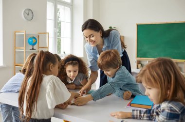 Modern sınıfta ilginç dersler alan mutlu öğretmen ve öğrenciler. Küçük çocuklar kitap okuyor, resimlere bakıyor, öğreniyor, yeni şeyleri tartışıyor, birlikte yaratıcı proje üzerinde çalışıyorlar.