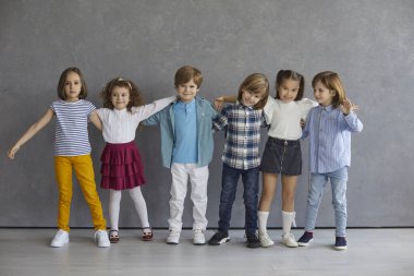 Neşeli küçük arkadaşlar bir araya geldi. Stüdyo grubunun altı mutlu gencin portresi. Gri duvarın yanında dikilmiş, sarılmış, gülümseyen ve kameraya bakan sevimli çocuklardan oluşan bir takım.