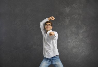 Neşeli genç adam, zafer ve başarıyı kutlayan gri bir arka planda tasasız dans eder. Neşeli adam elini kaldırarak atlayan neşe ve enerjiyi hisseder. Olumlu insani duyguların kabul edilmesi.