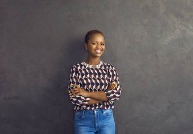 Olumlu duygular. Gri arka planda duran güzel gülümseyen Afrikalı Amerikalı kadının stüdyo portresi. Kısa saçlı, sıradan elbiseli genç bir kadın kameraya bakarak samimi bir şekilde gülümsüyor..