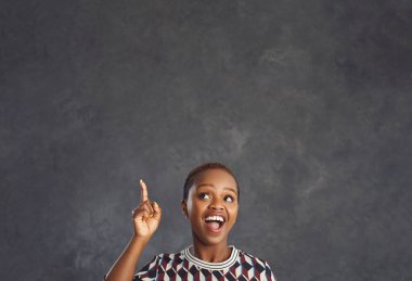 Benim bir fikrim var. Duygusal esmer kadın, parlak bir fikir ya da düşünceyle ortaya çıktığının işareti olarak işaret parmağını kaldırır. Gri arka planda bir kadın yazı için boş bir alana bakıyor.