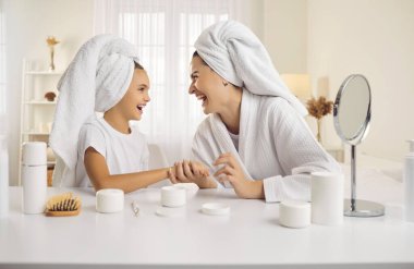 Mutlu anne ve küçük kızı sabah güzellik rutininin tadını çıkarıyorlar. Anne ve genç kız kafalarında havluyla oturuyor ve evde estetik ameliyatlar sırasında kahkahalarla gülüyorlar..