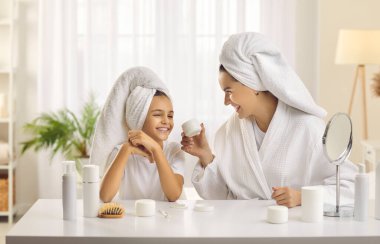 Genç, güzel anne ve küçük kızı sabah güzellik tedavilerinde eğleniyorlar. Beyaz banyo havlularına sarılı beyaz saçlı beyaz kadın ve genç kız evde güzellik günü düzenliyorlar..
