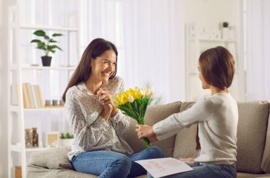 Sevgi dolu kız, Anneler Günü 'nde ona bir buket çiçek ve el yapımı kart vererek annesini tebrik eder. Mutlu genç anne, oturma odasındaki kanepede otururken hediyeleri ve selamları kabul eder..