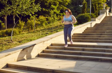 Artı boy, şişman kadın şehir parkında merdivenlerde koşuyor, dışarıda antrenman yapıyor ya da spor koşuyor. Koşu egzersizi ve sağlığın önemini vurgulayan aşırı kilolu kadın konumu.