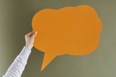 Kimliği belirsiz yetişkin bir kadın, turuncu bir bulut şeklinde, telif-uzay konuşma balonu ya da mesaj balonunu grimsi yeşil arka planda taklit ediyor. Fikir beyan etmek için boş ve temiz bir alanı olan el ele tutuşma kağıdı.