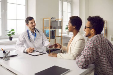 Mutlu siyahi evli çift aile doktoruna gidip danışmanlık yapıyor. Pratisyen hekim hastalara terapi reçetesi veriyor. Sağlıklı genç karı ve koca iyi sağlık muayenesi sonuçları alır.