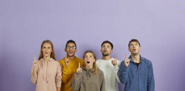Farklı melez ırktan çok ırklı insanlar. Renkli arka planda duran ve işaret parmaklarını açık ağızlarla ve şaşırmış yüz ifadeleriyle işaret eden harika bir fikir ve parlak bir çözümle sarsıldılar.