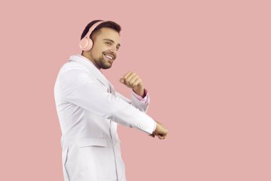 Aşırı neşeli takım elbiseli genç adam pembe stüdyo arka planında izole edilmiş kablosuz kulaklık takıyor müzik dinliyor. Kulaklıklı gülümseyen adam modern cihazda iyi kalite sesten hoşlanır. Teknoloji.