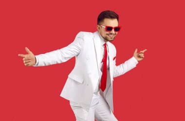 Zarif beyaz parti elbisesi ve kırmızı arka planda yalnız dans eden modaya uygun gözlüklü yakışıklı esmer adam. Mutlu MC 'nin stüdyo çekimi, sunucu, TV sunucusu, aktör, şarkıcı veya dansçı.