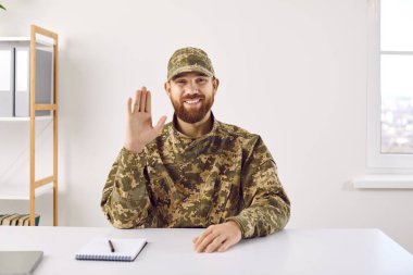 Asker çevrimiçi konferans yapıyor. Kamuflaj üniformalı sakallı bir adam askeri merkezdeki masada oturuyor gülümsüyor, kameraya bakıyor ve el sallıyor. Mutlu baba videosu ailesini arıyor.