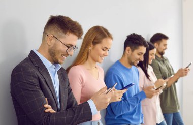 Cep telefonu kullanan mutlu gençler. Milenyum erkek ve kadınların bir arada durması, cep telefonlarını tutmaları, duvara yaslanmaları, ücretsiz kablosuz internete bağlanmaları, haber yayınları, haberleri okumaları ve gülümsemeleri.