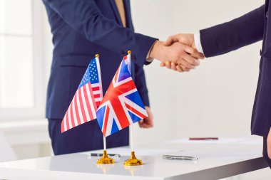 İngiltere ve Amerika 'dan diplomatlar ofiste bir araya geldiler, ikili ticaret anlaşmasına vardılar, iş sözleşmesi imzaladılar ve ABD ve İngiltere' nin ulusal bayraklarıyla müzakere masasında el sıkıştılar.