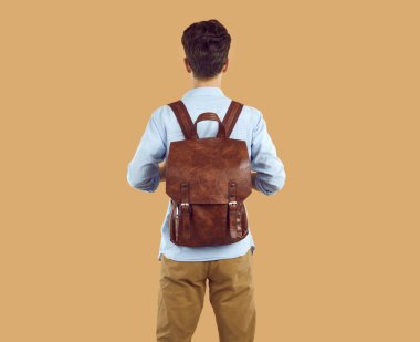 Sırt çantalı genç adamın nadir görüntüsü. Esmer, eski tarz deri sırt çantalı, izole stüdyo arka planında poz veren sıradan giyinmiş bir adamın portresi.