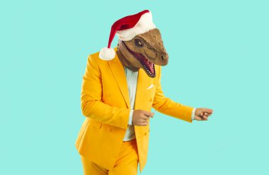 Sarı takım elbiseli komik şovmen portresi, Noel Baba şapkası ve turkuaz arka planda dans eden lastik dinozor maskesi ve parmaklarını şıklatıyor. Noel Xmas reklamı için pankart, funky adamla pazarlama.