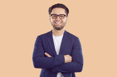 Koyu takım elbiseli, gülümseyen, hoş, genç bir iş adamı. Koyu renk saçlı, sakallı ve gözlüklü yakışıklı. Kolları çaprazlanmış. İzole edilmiş bir arkaplanda stüdyonun yakın plan çekimi.