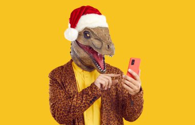 Noel şapkalı, cep telefonu kullanan komik, heyecanlı dinozor adam. Tuhaf tuhaf dino kertenkele maskesi, leopar ceketi ve Xmas şapkası takan akıllı telefon takan ve mesaj gönderen erkek manken.