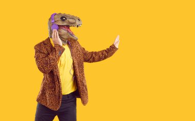 Lastik dinozor maskeli tuhaf komik bir şovmen mor kulaklıklı müzik dinliyor ve sarı arka planda fotokopi alanında elini gösteriyor. Sarı gömlek, siyah pantolon ve leopar ceket giyiyor..
