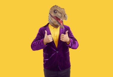 Lastik dinozor maskeli, mor kadife ceketli, sarı gömlekli, sarı arka planda baş parmağını gösteren komik bir şovmen. Reklam afişi, funky adamla pazarlama. Parti, maskeli balo.