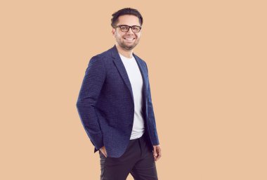 Mavi ceketli, kot pantolonlu, beyaz tişörtlü ve bej arka planda el ele tutuşup kameraya bakan gülümseyen esmer işadamının portresi. Samimi duygular, vücut dili kavramı.