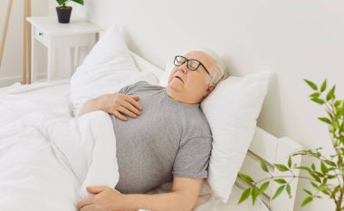 Yaşlı bir adam evdeki yatak odasında rahat bir şekilde dinleniyor, ferahlatıcı bir uyku çekiyor. Bu sakin sabahın erken saatleri memnuniyeti ve güne huzurlu bir başlangıcı yansıtıyor..