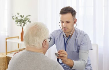 Kendine güvenen bir doktor ya da bakıcı, hastanede yatan yaşlı bir adamın ciğerlerini ve nefesini dinlemek için steteskop kullanır. Sağlık, hasta bakımı ve solunum muayenesi..