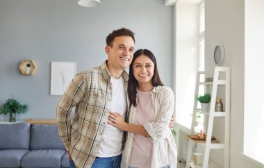 Evdeki oturma odasında, sıradan giysiler içinde sarılan neşeli genç bir adam ve kadının portresi. Aşık mutlu bir çift. İlişkiler, romantizm ve Sevgililer Günü konsepti.