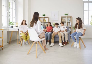 Dost canlısı genç psikolog bir grup genç çocukla sohbet ediyor. Okul öğrencileri, kadın öğretmenle kanepede oturup akıl sağlığı dersi alıyorlar. Psikoloji konsepti.