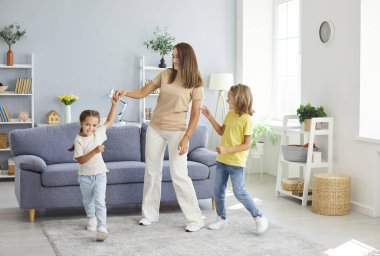 Evdeki oturma odasında eğlenen ve dans eden anne ve iki çocuğun genç mutlu portresi. Çocuklarla vakit geçirmekten hoşlanan bir kadın. Aile eğlencesi ve anneler günü konsepti