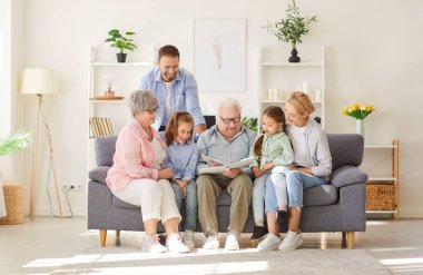 Mutlu bir büyükbabanın portresi. Torunlarına aile albümünü gösteriyor. Evdeki kanepede oturuyor. Ebeveynler, büyük ebeveynler ve çocuklar hafta sonları birlikte vakit geçiriyorlar..