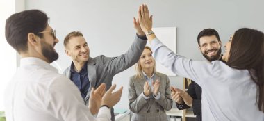 Grup ve takım halinde mutlu bir iş adamı grubu ofis toplantısında birlikte çalışır, başarıyı kutlamak için beşlik çakar, neşe ve çaba ile profesyonel bir ortamda takım çalışması sergiler..
