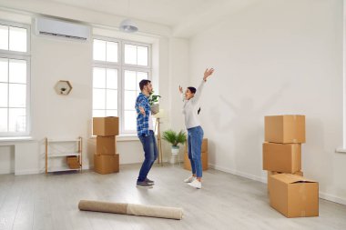 Yeni daireye taşınmayı kutlayan heyecanlı genç bir çift. Mutlu karı koca, modern oturma odasında karton kutularla eğleniyor. Ev taşınması, aile konutları, gayrimenkul