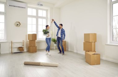 Taşındıkları gün evlerinde dans eden mutlu çift. Heyecanlı eşler ev sahipleri modern oturma odasında karton kutuların arasında eşyalarıyla eğleniyorlar. Ev taşınması, ipotek, gayrimenkul