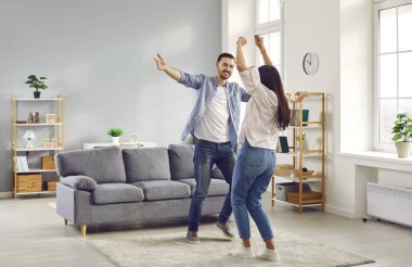 Mutlu aile çifti birlikte eğleniyor ve evdeki oturma odasında dans ediyor. Genç adam ve kadın neşeli bir şeyi kutluyorlar. Yeni bir daire almak ya da ipoteği erken ödemek gibi.