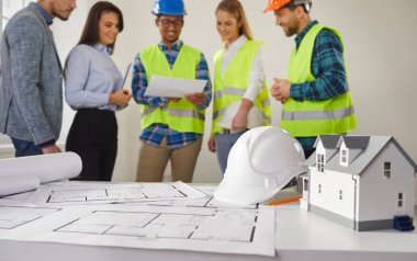 Çeşitli etnik çeşitlilikte mimarlar, iç mimarlar ve işçiler inşaat projesiyle ilgili proje üzerinde tartışıyorlar. Mimari planın mühendis teftişi