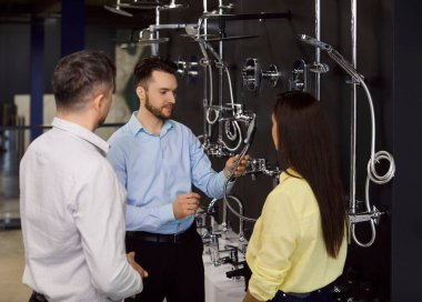 Erkek mağaza asistanı aile çiftleri için musluk ya da duş öneriyor. Tesisatçı dükkanında poz veriyor. Kadın ve erkek banyo yenileme için musluk seçiyor, iyi müşteri hizmetlerinden memnun.