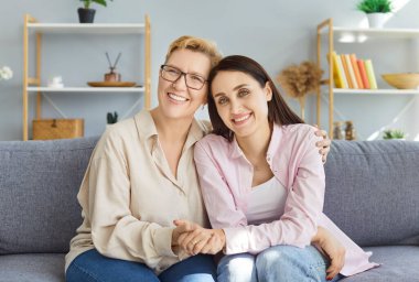 Mutlu gülümseyen yetişkin bir kızın portresi. Yetişkin anne babasıyla kucaklaşıyor. Kanepede dinleniyor ve kameraya neşeli bakıyor. Sevgi, aile ve anneler günü konsepti.