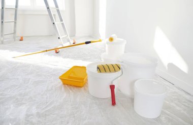 Arka planda yeni boyanmış merdivenli beyaz duvarları olan boş bir evde boya rulosu olan kovaları kapatın. Evdeki yenileme işlemi. Ev onarımı ve taşınma günü konsepti