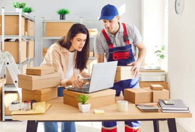 Kadın ve erkek bir paket ambarında birlikte çalışıp dizüstü bilgisayar kullanarak envanter çıkarıyorlar. Takım çalışması ve paket ve paketlerin verimli yönetimi iş operasyonlarına olan bağlılığı vurguluyor.