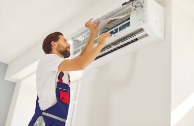 Havalandırma tesisatı işçisi ve modern kapalı oda havalandırma ünitesini yeni daire veya ofisin içinde bir şeyleri tamir eden ya da eski temizleyici parçalarını kaldıran bir oda duvarına kuran garanti hizmetlisi.