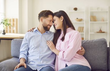 Evdeki oturma odasındaki kanepede oturan mutlu evli çiftin portresi. Kanepede birbirine bakan gülümseyen aile babası ve kadın. Ahenkli ilişkiler kavramı.