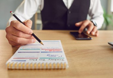 İş adamının görev yazarken çekilmiş fotoğrafı ve masa başında elinde akıllı telefonla otururken ya da ofis planlama programında günlük randevularını planlarken. Planlayıcı konsepti.
