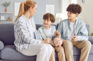 Pozitif ve gülümseyen anne iki oğluyla birlikte evdeki kumbaraya bozuk para koyuyor. Aile birliği ve para biriktirmenin önemi, bir aile olarak finansal zenginlik inşa etmek..