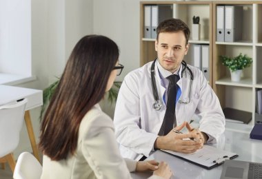 Kendine güveni tam genç bir erkek doktor, klinikteki muayene odasında çalışan kadın hastasına danışıyor ve muayenehanede tedavi önerilerinde bulunuyor. Tıp konsepti.
