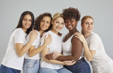 Birbirlerine yakın gri duvara yaslanmış mutlu melez kadınların görüntüsü ve birbirlerine sarılıp doğrudan kameraya bakmaları dişlek bir gülümsemeye ve temiz bir cilde sahip olmaları. Kadın güzellik konsepti