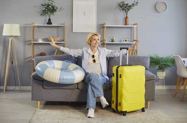 Happy woman packing a suitcase and enjoys the anticipation of a summer vacation while sitting on a sofa at home. Trip preparation and holiday excitement create a joyful atmosphere.