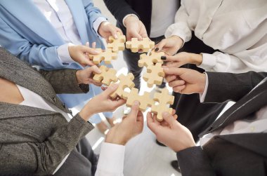 Tahta yapboz yapan bir grup iş adamının elleri. İş arkadaşları, ofis içindeki yapboz parçalarına katılıp proje üzerinde birlikte çalışıyorlar. Takım çalışması konseptinde destek.