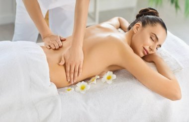 Masaj masasında gözleri kapalı uzanan memnun bir kadın. Bu arada profesyonel masöz de lüks bir kaplıcada sırt masajı yapıyor. Kendini rahat ve rahat hissediyor.