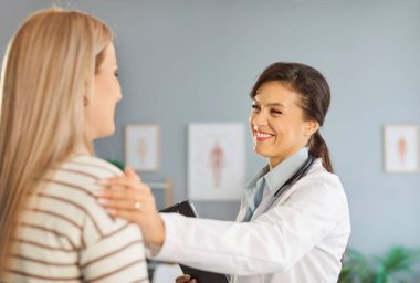 Neşeli bir kadın doktorun portresi, elini omzuna koyan gülümseyen bir hastaya destek oluyor. Muayene sırasında bir kadınla klinikte doktor. Tıp konsepti.